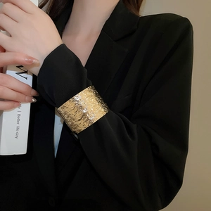 Macro shot of wide golden hammered texture metal cuff bracelet on black suit sleeve