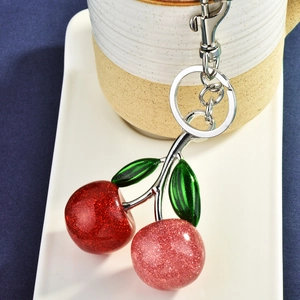 Glittering cherry keychain with red rhinestones and silver metal clasp on white tray