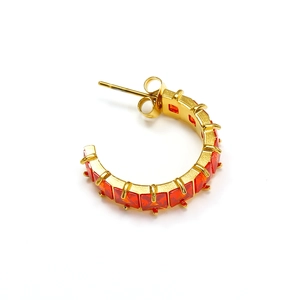 Detail of C-shaped gold earrings featuring channel-set red square zircon stones