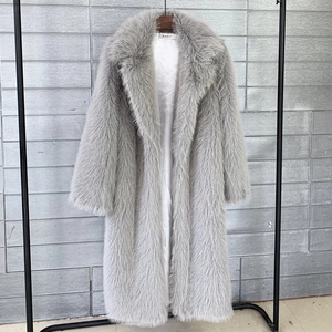 Close-up of light gray faux fur coat with lapel collar hanging on a rack against a wall
