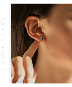 Macro shot of silver heart stud earrings with blue opal and halo stones on ear