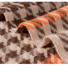 Macro shot showing soft houndstooth texture and fringe detail on a warm cashmere scarf