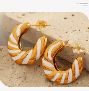 Macro detail of gold geometric hoop earrings with white enamel spiral texture