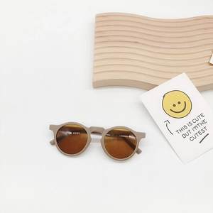 Close-up of beige round kids sunglasses on a wooden stand with a cute decorative card