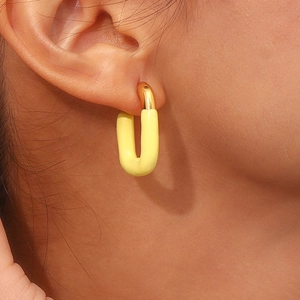 Close-up of U-shaped gold earrings with bright yellow enamel on model ear