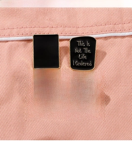 Detail of four black enamel badges with gold edges on pink denim fabric background