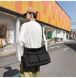 Street style shot of black canvas messenger bag with double pockets and wide strap