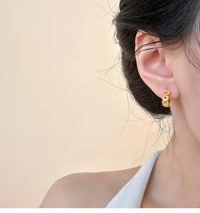 Close-up of gold-plated circular coin-shaped hoop earrings worn by a model in soft light