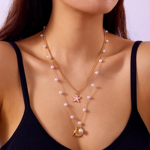 Close-up of double layer gold necklace with pink starfish, shell and pearl charms on model