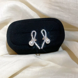 Close-up of silver bow-knot pearl earrings with sparkling zircons on black velvet