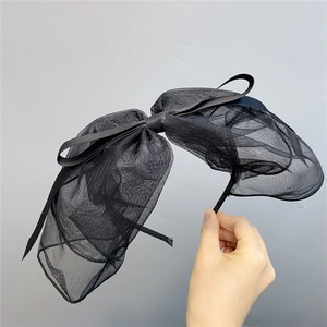Detail view of the black oversized polka dot mesh bow headband held by a model