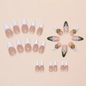 Detail of almond press-on nails featuring 3D white flowers, gold beads and green accents