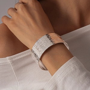 Detailed close-up of wide silver cuff bracelet with vintage floral relief patterns