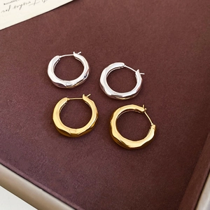 Macro detail of textured gold and silver hoop earrings with a wavy metal finish