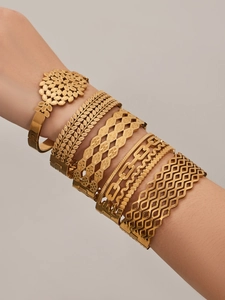 Detail view of stacked gold leaf cutout and textured metal bracelets on a model's wrist