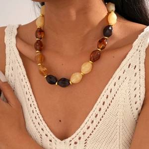 Detailed view of an oval acrylic beaded necklace in beige, amber and black with gold accents