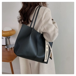 Detail of a large black faux leather tote bag with a decorative fashion strap on model