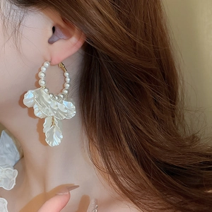 Close-up of pearl and white petal pendant earrings worn by a model in soft light
