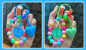 Dettaglio di portachiavi a cuore con perline colorate e lettere, tenuti in mano.