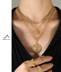 Detail of layered gold stainless steel necklace with moon and lion head coin pendants