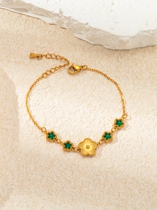 Detail of gold bracelet featuring green star gemstones and central floral charm decoration