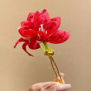 Vue détaillée d'une élégante épingle à cheveux fleur en tissu rouge avec des gouttes d'eau
