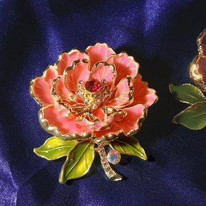 Détail macro d'une broche pivoine en émail rose avec bords dorés et zircons sur soie