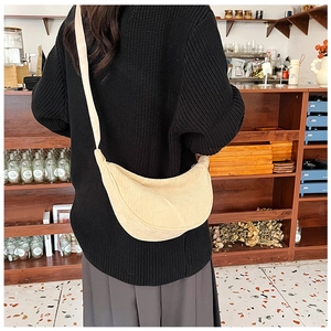 Beige corduroy crescent crossbody bag shown on a model in a cozy cafe setting