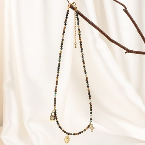 Detail of beaded gemstone necklace with gold cross and medallion on a natural wooden branch