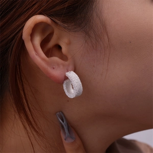 Close-up of frosted silver C-shaped geometric earrings with sparkling matte texture