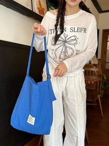 Royal blue pleated canvas tote bag worn by a model in a cozy indoor cafe setting