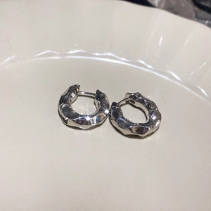 Close-up of silver irregular hammered geometric stud earrings on a beige ceramic plate