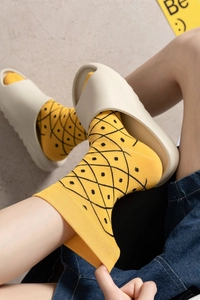 Detail shot of yellow crew socks with black pineapple pattern worn with beige slippers