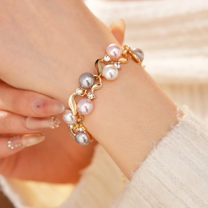Détail d'un bracelet doré vintage avec perles roses, grises et blanches et strass étincelants