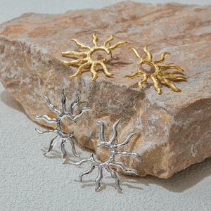Macro shot of gold and silver sunburst geometric earrings on a textured stone base