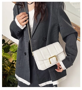 Detail view of quilted white shoulder bag with golden chain strap on a grey blazer
