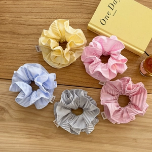 Close-up of five striped fabric hair scrunchies with brand labels on a wooden table
