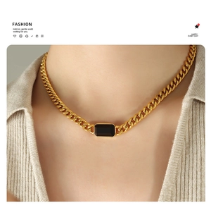 Detail of chunky gold Cuban chain necklace featuring a rectangular black gemstone on model