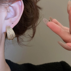 Close-up of gold layered C-shape earrings with textured woven metal design on model