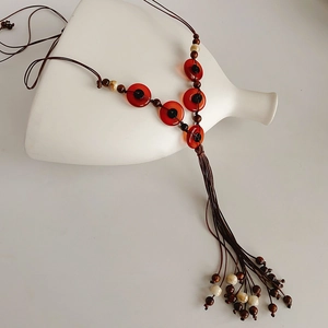 Detail of bohemian necklace with red resin beads and wood elements on a ceramic vase