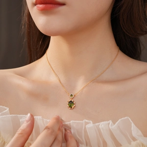 Macro shot of gold-plated necklace with oval green gemstone and zircon butterfly details