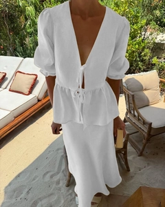 Detail of white V-neck ruffle crop top and midi skirt set on tropical beach background