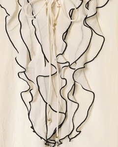 Dettaglio della camicetta bianca a balze con scollo a V e finiture nere eleganti