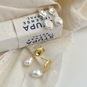 Detail of irregular baroque pearl earrings in gold and silver finish on linen fabric