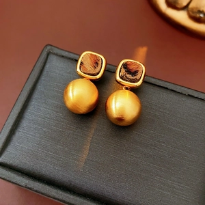 Macro shot of brown leopard print earrings on black jewelry box with matte gold pendants