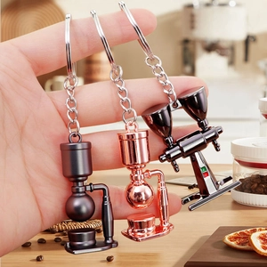 3D miniature coffee maker metal keychains in rose gold and gunmetal finishes held in hand