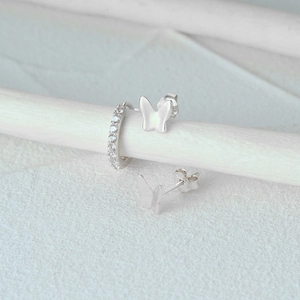 Detail of silver earring set with butterfly studs and zircon-encrusted hoop on white stand