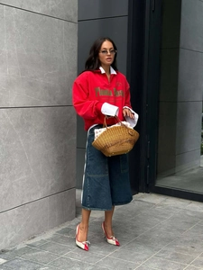 Outdoor street shot of red half-zip sweatshirt with green lettering and denim wide-leg pants