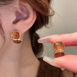 Close-up of amber resin square earrings with gold plating on model and in hand