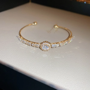 Close-up of gold-plated open bangle with cubic zirconia flower and baguette-cut stones